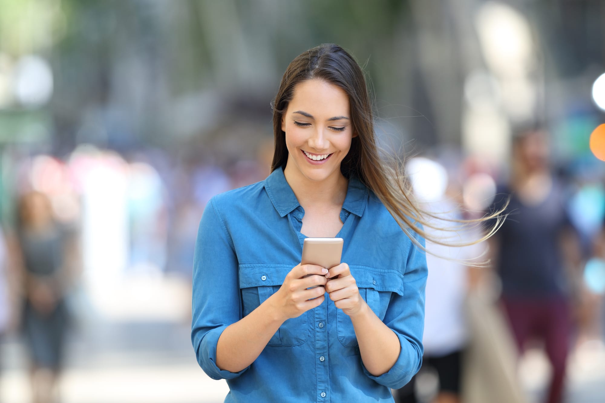 Eine Frau auf einer belebten Straße schaut lächelnd auf ihr Smartphone