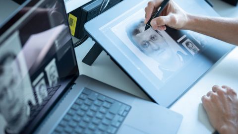 A person draws a sketch on a tablet. Next to the tablet is a laptop on which sketches can be seen.